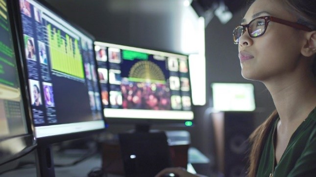 Lady in glasses sitting in front of various computer moniitors