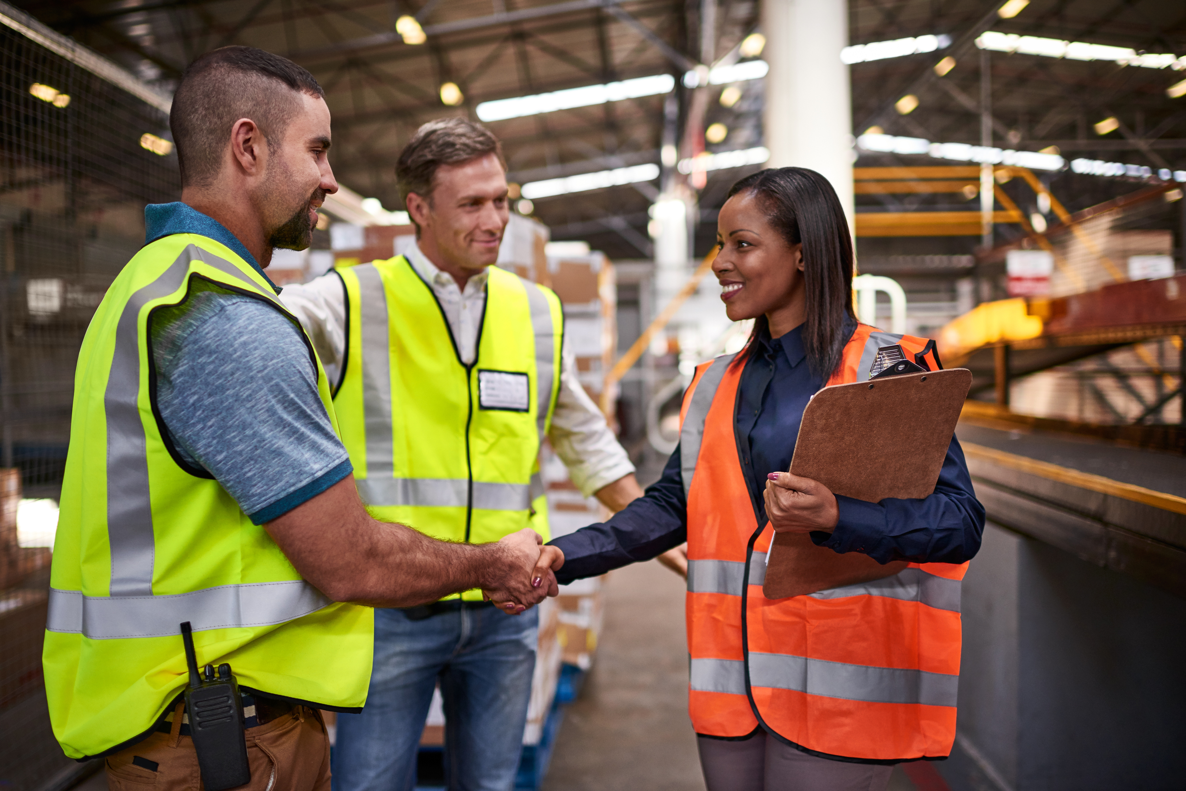 Woman greeting two men in high vis in a factory