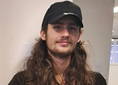 Inside an office, Elias stands dressed in black next to an Asuria stand-up banner.