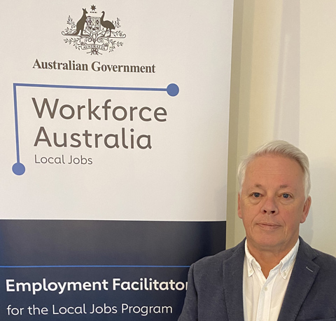 Sean Teer, Employment Facilitator for South-East Melbourne and Peninsula, looking calmly at the camera while standing in-front of a Workforce Australia banner.