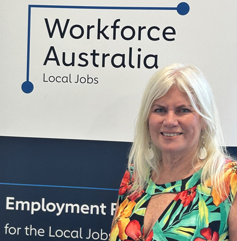 The Australian Government Employment Faciliator for South West WA stands grinning in front of a Workforce Australia banner.