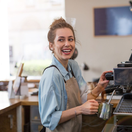 A barista using a professional coffee maker is looking over her shoulder with a look of joy on her face