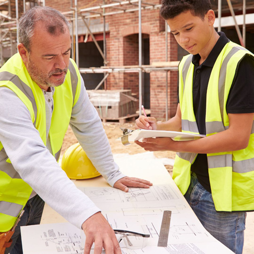 Two men dressed in high visibility vests are looking down on a table, examining documents. The men are located outside in a building site.