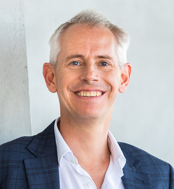 Close-up of Andrew Giles looking at and smiling at the camera in front of a grey background.