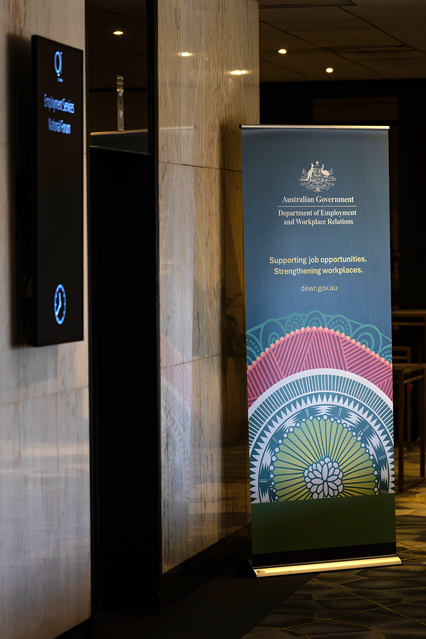 A pop-up banner is positioned next to a Mahogony wall inside a function room. On the banner is the text "Australian Government Department of Employment and Workplace Relations – Supporting job opportunities. Strengthening workplaces. dewr.gov.au"