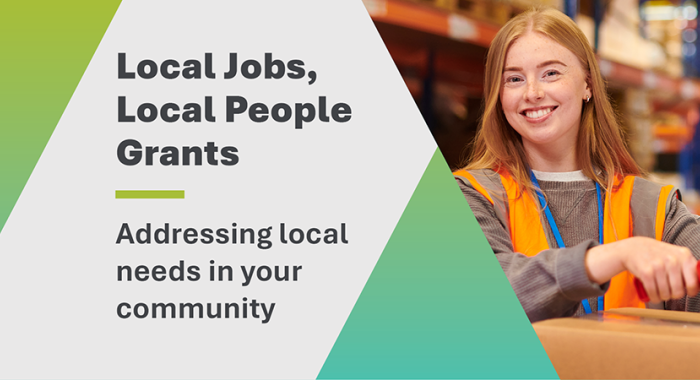 Mid-shot of a young woman in high-visibility orange workwear, smiling at the camera while taping the top of a cardboard box. On the left side of the frame is the title: 'Local Jobs, Local People Grants – Addressing local needs in your community'