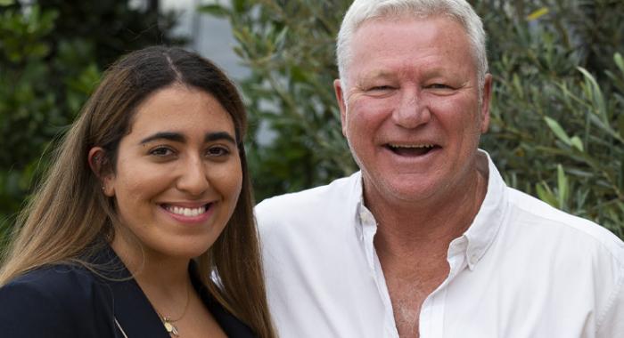 Mary has long brown hair and Scott has cropped white hair. Both are smiling happily at the camera.