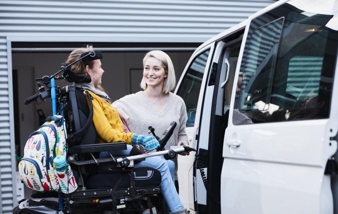 A career helping a young woman wearing a yellow jumper and positioned in a wheelchair to move into a van
