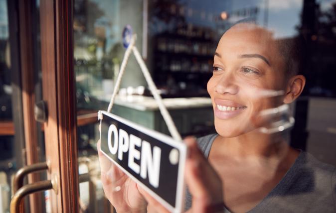Woman turning an open-closed sign on a glass entry door