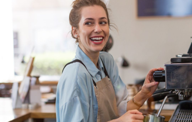 A barista using a professional coffee maker is looking over her shoulder with a look of joy on her face