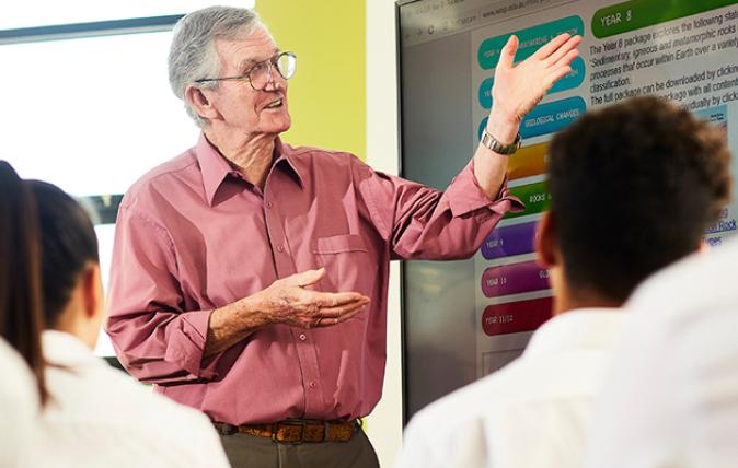 A teacher discussing education materials on a whiteboard with students in the foreground