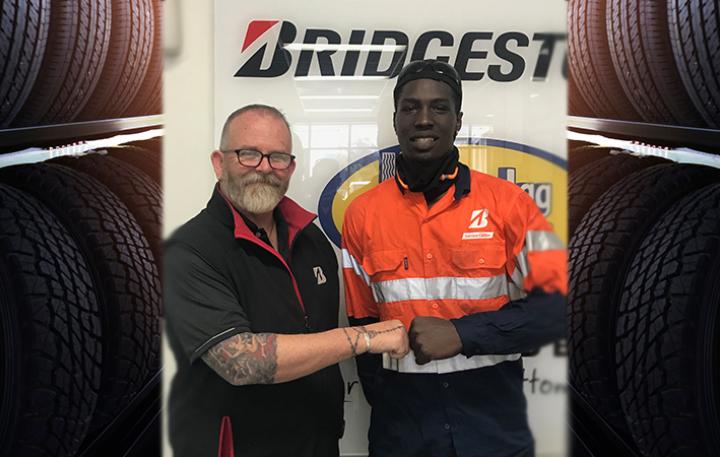 Two men shaking hands in front of Bridgestone sign