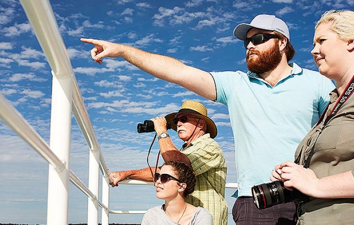 Five people standing on a boat enjoying the view. The sky is blue with white clouds