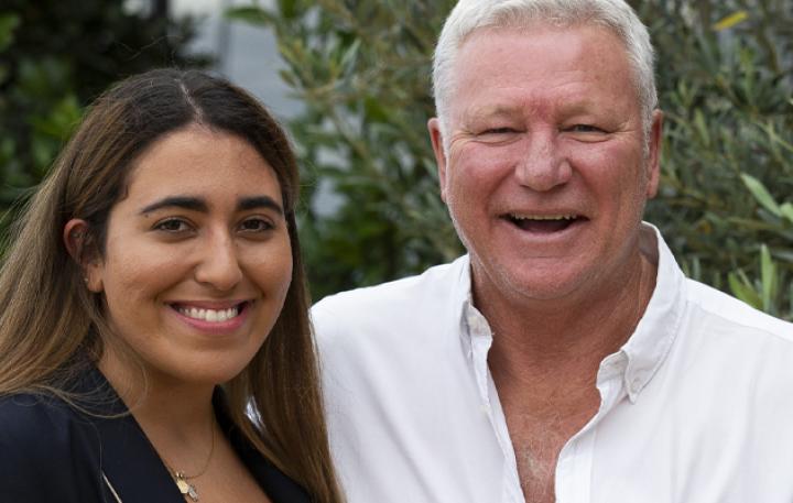 Mary has long brown hair and Scott has cropped white hair. Both are smiling happily at the camera.