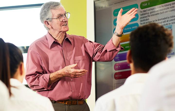 A teacher discussing education materials on a whiteboard with students in the foreground