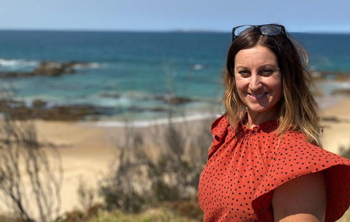 Business owner, Lee-Anne Eddie is standing on the sands of Mystery Bay with the blue ocean behind her. It is a bright and sunny day.