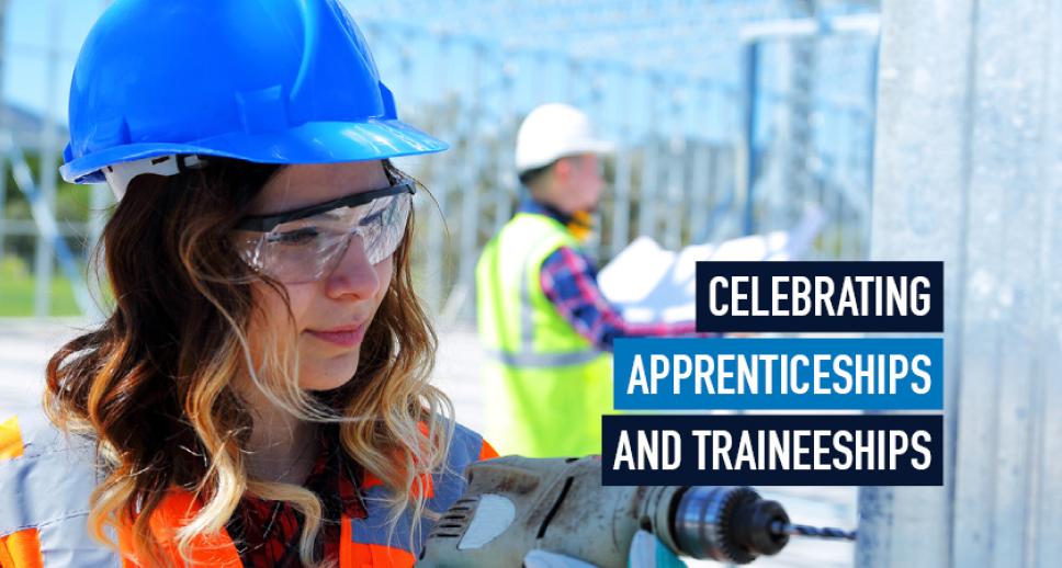 A young woman wearing a high-visibility vest and a blue safety helmet is on a work site drilling into a wall while a man in a similar outfit examines a layout document in the background. Superimposed next to the woman is the title 'Celebrating Apprenticeships and Traineeships'.
