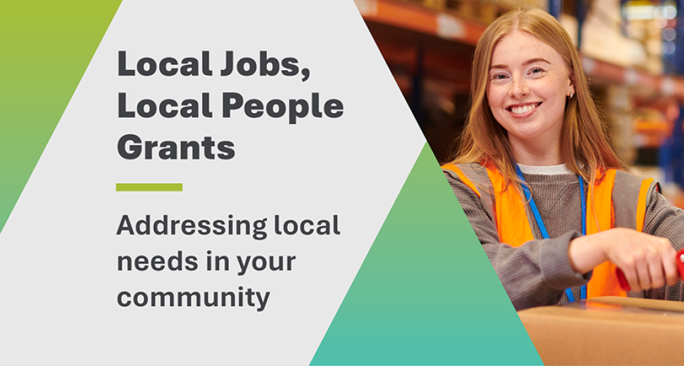 Mid-shot of a young woman in high-visibility orange workwear, smiling at the camera while taping the top of a cardboard box. On the left side of the frame is the title: 'Local Jobs, Local People Grants – Addressing local needs in your community'
